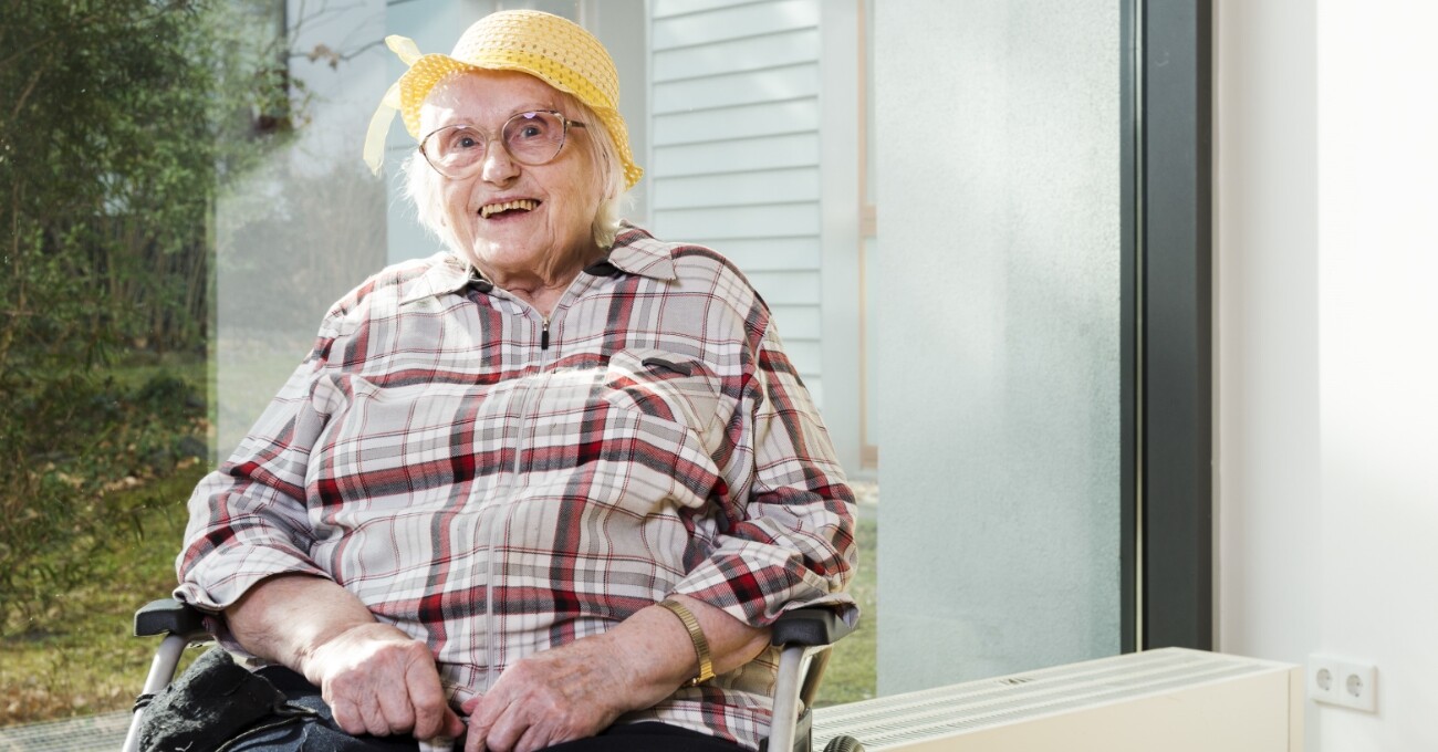 Eine ältere Dame mit Sonnenhut lächelt ihrem Gegenüber freundlich entgegen.