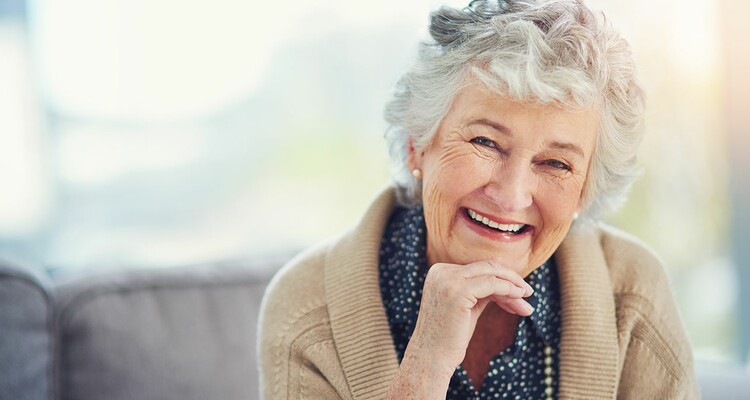 Eine ältere Dame lächelt glücklich in die Kamera.